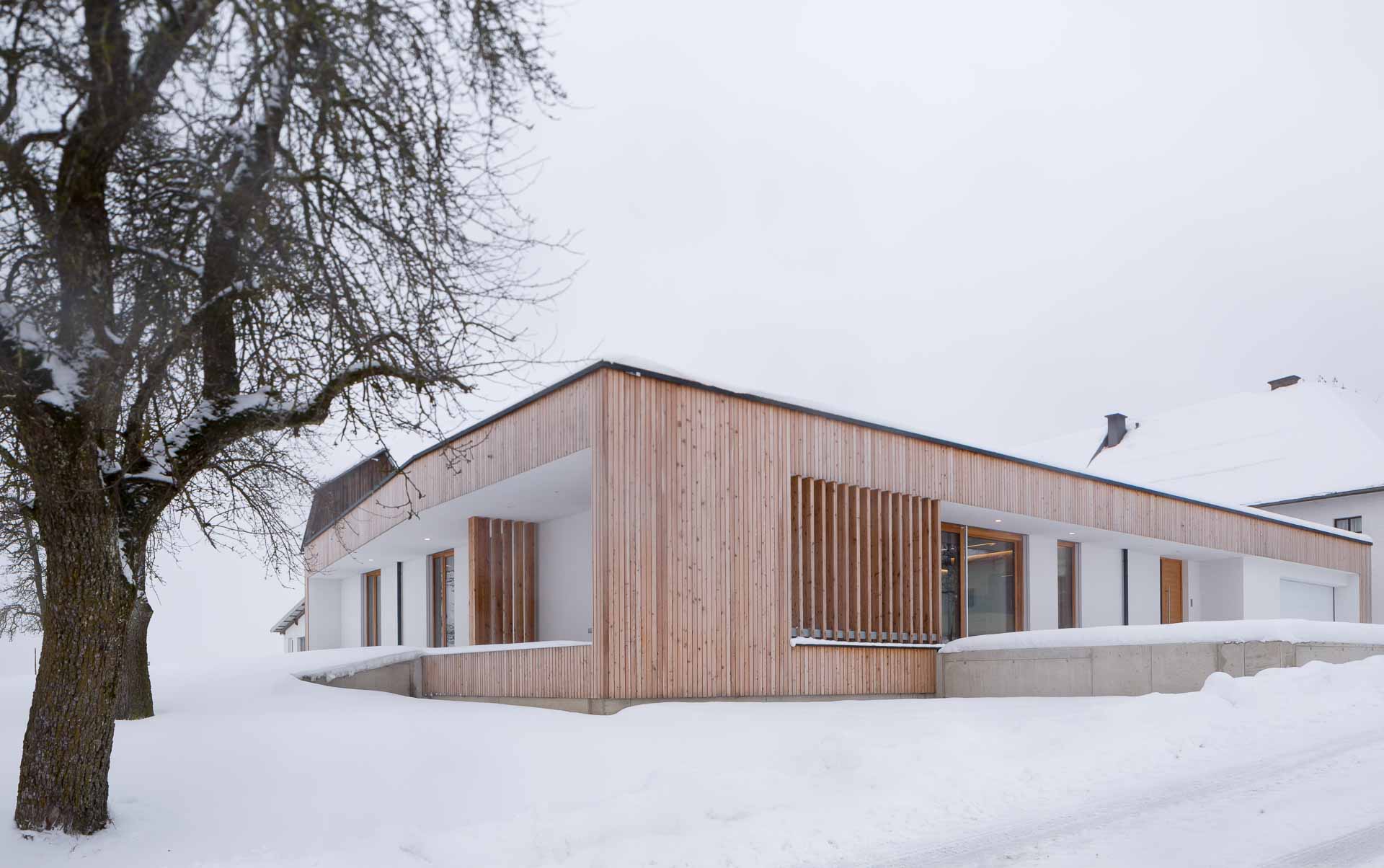 Architektur im Winter, Bungalow mit dicker Schneedecke, warme und kühle Farbtöne treffen sich, warmes Lärchenholz, moderne Architektur