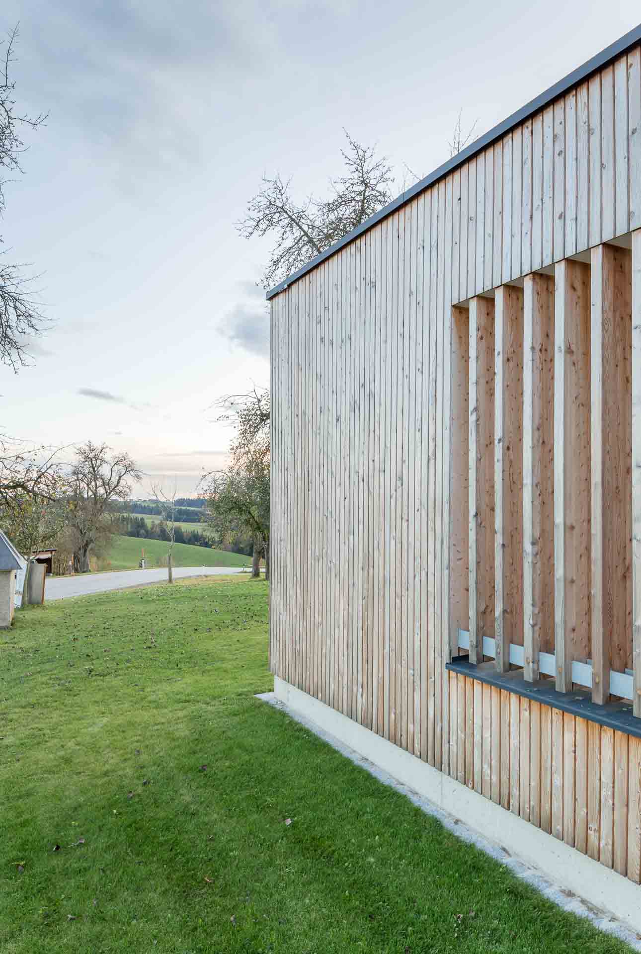 Gebäudeteil mit Holzfassade und Lamellen, lärchenholzfassade, leicht vergraut, Hausdetail, grüne Umgebung, Sonnenuntergang, schöne Abendstimmung,